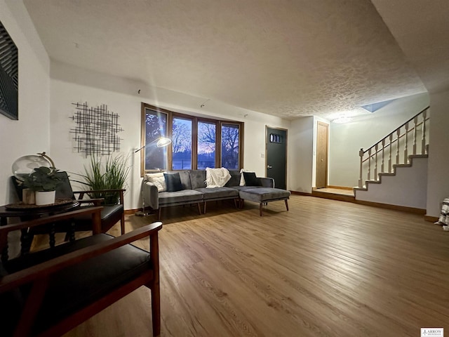 living room featuring stairs, a textured ceiling, wood finished floors, and baseboards