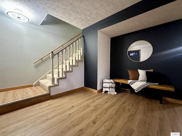 living area with a textured ceiling, stairway, baseboards, and wood finished floors