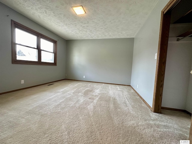 spare room with baseboards, a textured ceiling, and light colored carpet