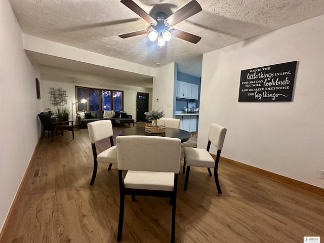 dining room with a ceiling fan, a textured ceiling, baseboards, and wood finished floors