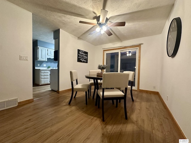 dining space with visible vents, a textured ceiling, baseboards, and wood finished floors