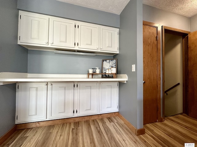 kitchen featuring a textured ceiling, light countertops, light wood-style flooring, and white cabinetry