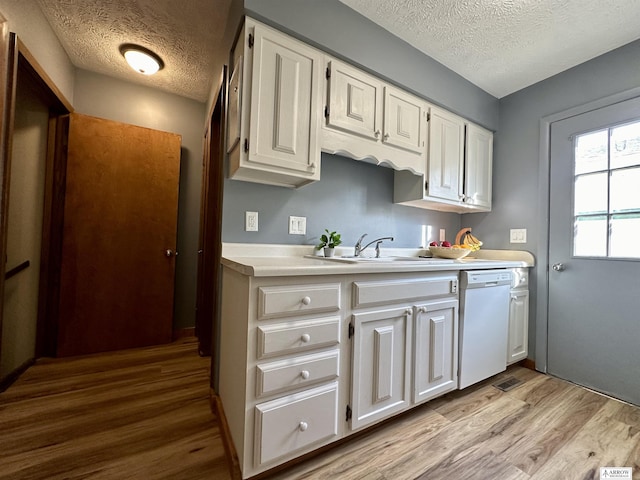 kitchen featuring white cabinets, dishwasher, light countertops, light wood-style floors, and a sink