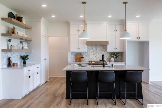 kitchen featuring white cabinets, pendant lighting, a kitchen island with sink, light countertops, and open shelves