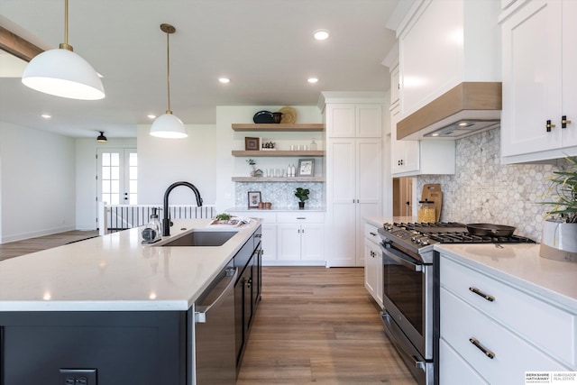 kitchen with hanging light fixtures, custom exhaust hood, stainless steel appliances, open shelves, and a sink