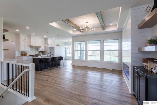 kitchen with a chandelier, an island with sink, a breakfast bar, white cabinetry, and pendant lighting