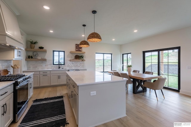 kitchen featuring white cabinets, hanging light fixtures, stainless steel range with gas cooktop, a center island, and open shelves