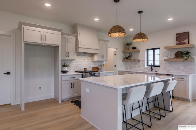 kitchen featuring premium range hood, white cabinets, a center island, open shelves, and decorative light fixtures