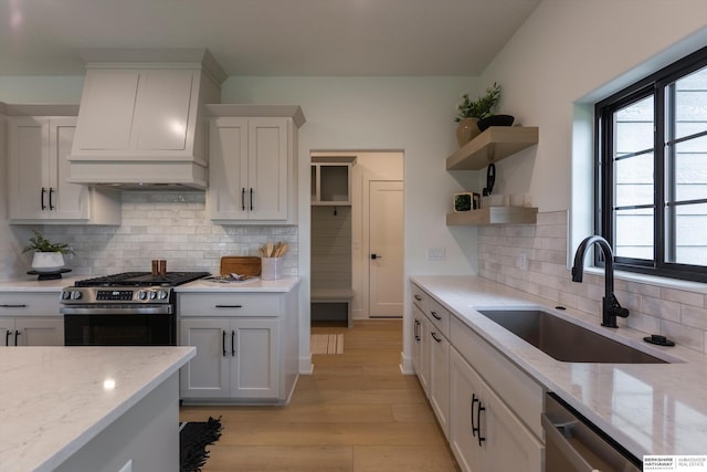 kitchen with stainless steel appliances, a sink, light stone countertops, and custom range hood