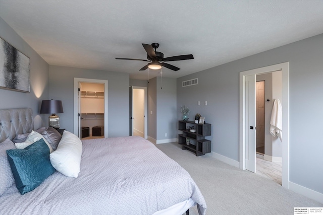 bedroom with a walk in closet, a closet, visible vents, light carpet, and baseboards