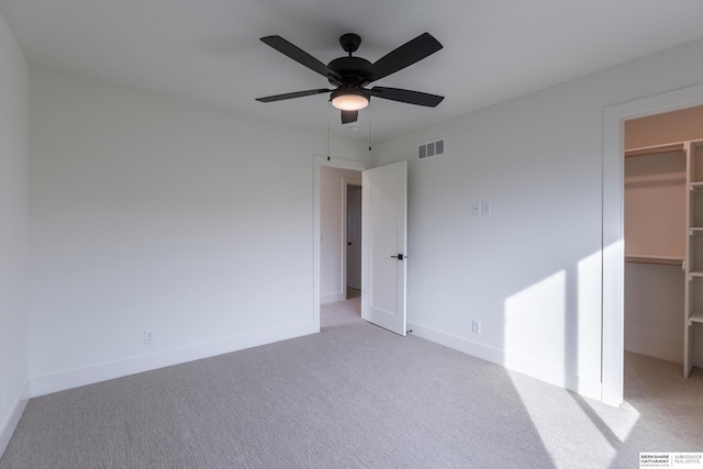 unfurnished bedroom featuring light carpet, baseboards, visible vents, and a walk in closet