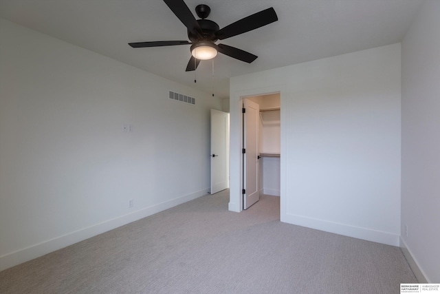 unfurnished bedroom with ceiling fan, light colored carpet, visible vents, baseboards, and a walk in closet