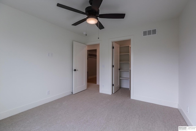 unfurnished bedroom with light carpet, visible vents, baseboards, a closet, and a walk in closet