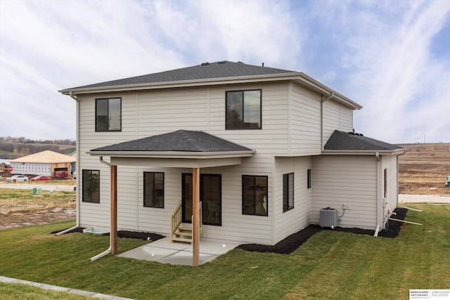 back of property with entry steps, central AC, a shingled roof, a yard, and a patio area