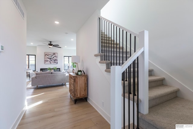 staircase featuring a large fireplace, baseboards, visible vents, wood finished floors, and recessed lighting