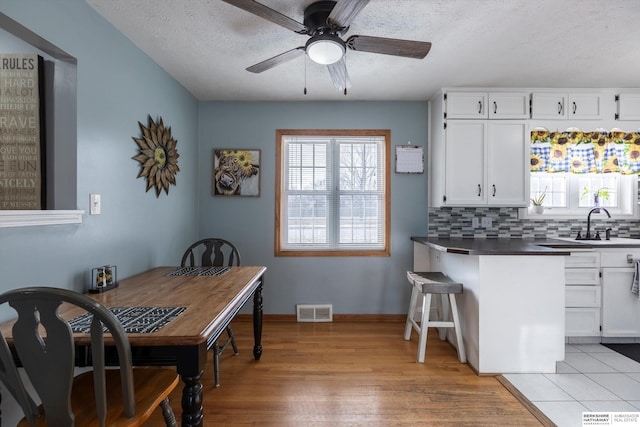 kitchen with tasteful backsplash, visible vents, white cabinets, dark countertops, and light wood-style flooring