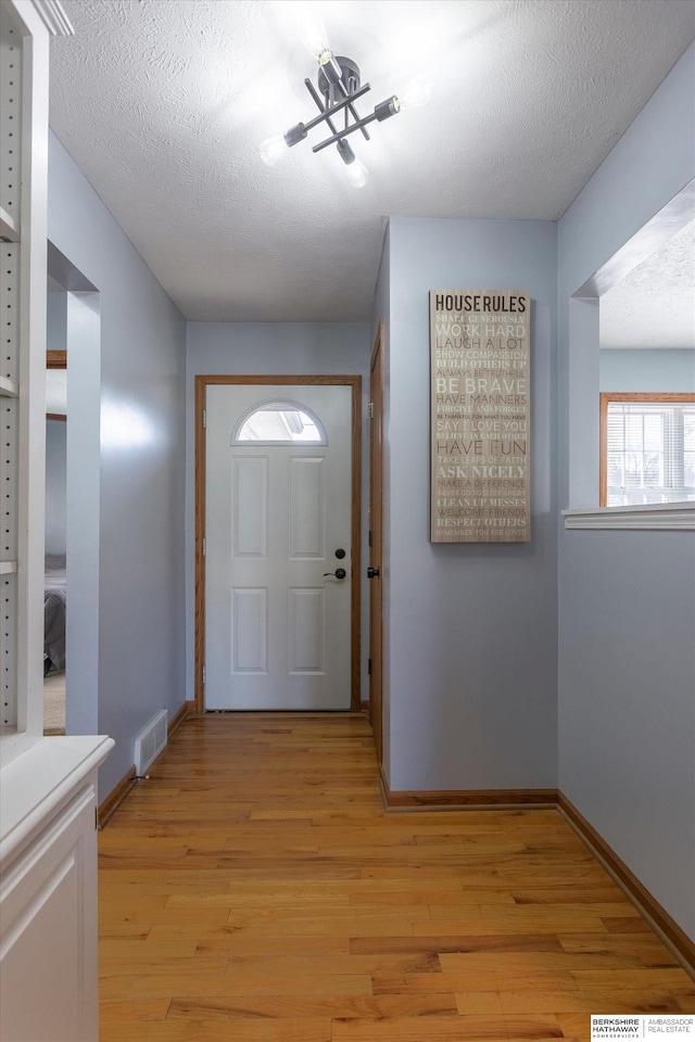 entryway with a textured ceiling, light wood finished floors, visible vents, and baseboards