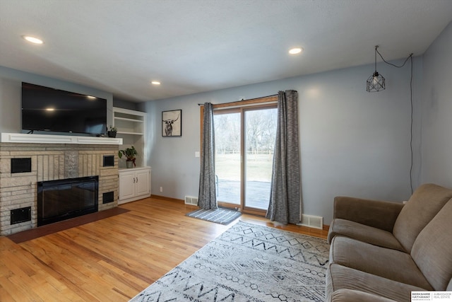 living area featuring light wood finished floors, baseboards, visible vents, a fireplace, and recessed lighting