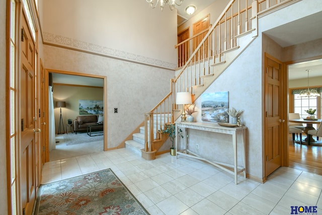 tiled foyer entrance featuring baseboards, a notable chandelier, a towering ceiling, and stairs