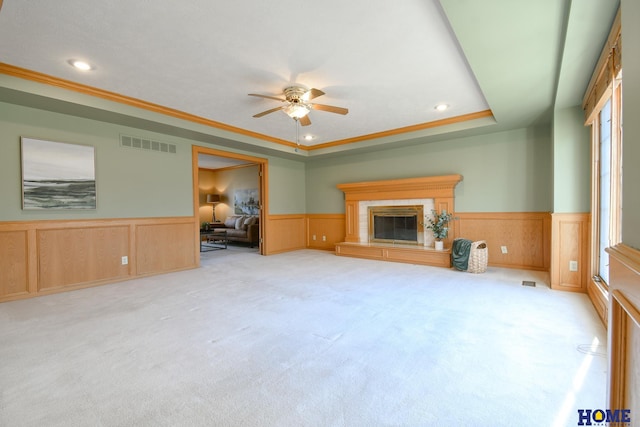 unfurnished living room with a glass covered fireplace, a wainscoted wall, visible vents, and a tray ceiling