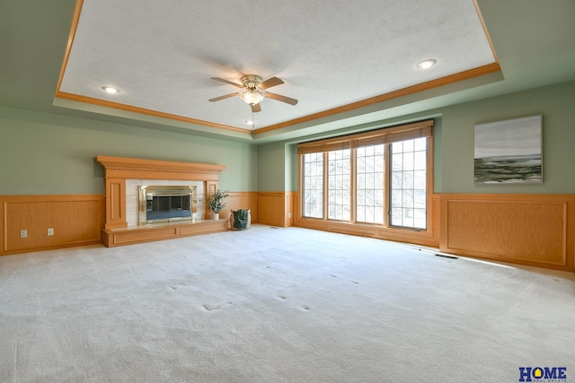 unfurnished living room featuring a wainscoted wall, a raised ceiling, and a tile fireplace