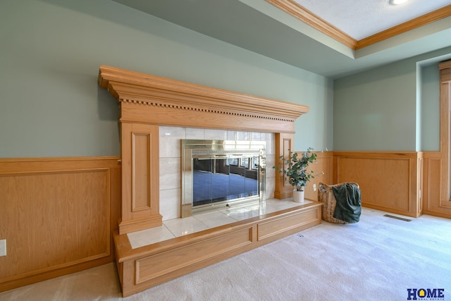 interior details with visible vents, a tiled fireplace, a wainscoted wall, carpet floors, and ornamental molding