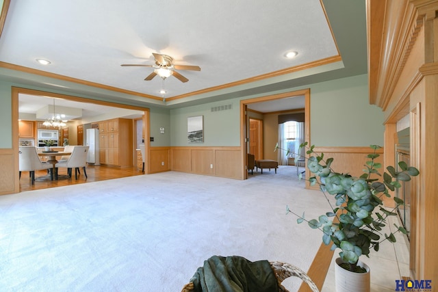 living room featuring a wainscoted wall, a raised ceiling, visible vents, and crown molding