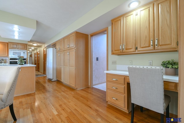 kitchen with light wood-type flooring, white appliances, built in desk, and light countertops