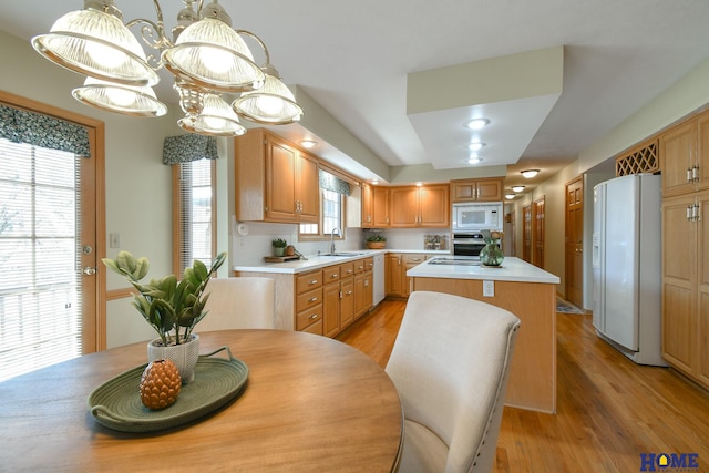 kitchen featuring white appliances, a sink, light countertops, light wood-type flooring, and a center island