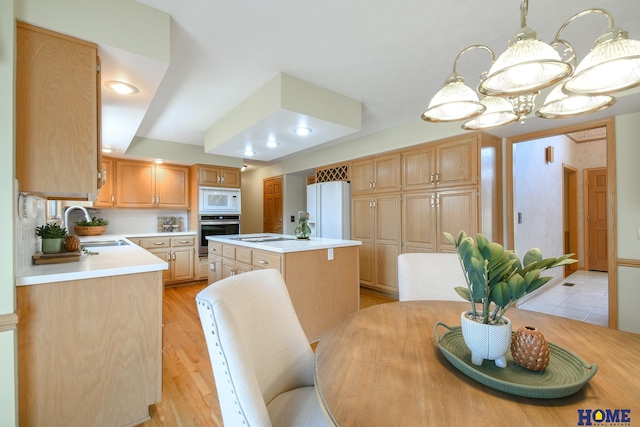 kitchen featuring white appliances, a kitchen island, a sink, light countertops, and light wood-type flooring