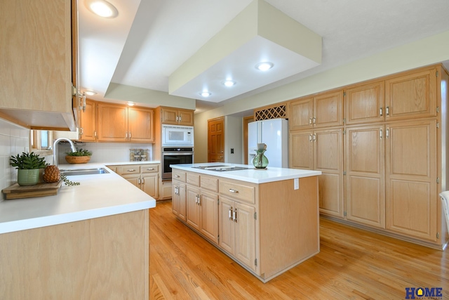 kitchen with light brown cabinets, a center island, light countertops, white appliances, and a sink