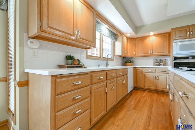 kitchen featuring light wood finished floors, backsplash, light countertops, white appliances, and a sink