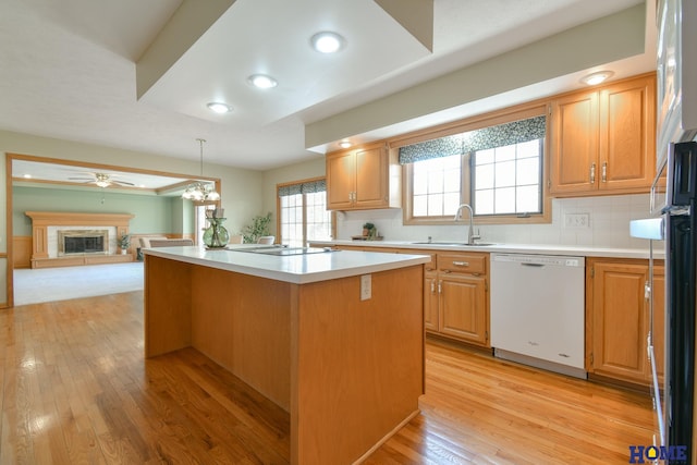 kitchen featuring a kitchen island, dishwasher, light countertops, a glass covered fireplace, and a sink