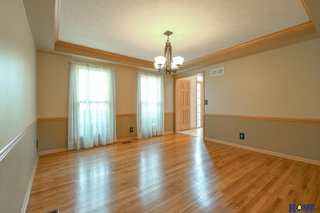 spare room featuring visible vents, light wood-type flooring, ornamental molding, an inviting chandelier, and a raised ceiling