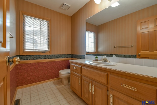 bathroom with wallpapered walls, toilet, wainscoting, tile patterned floors, and vanity