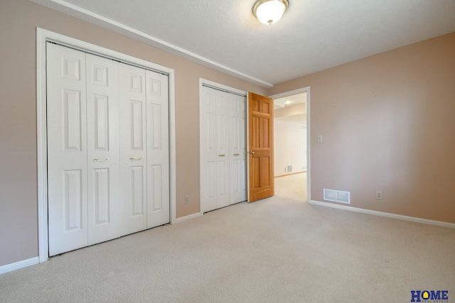 unfurnished bedroom with carpet, visible vents, two closets, and baseboards