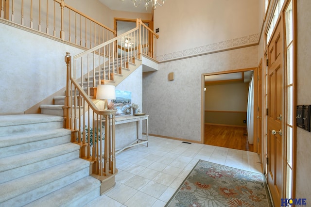 staircase with tile patterned floors, visible vents, baseboards, and a towering ceiling