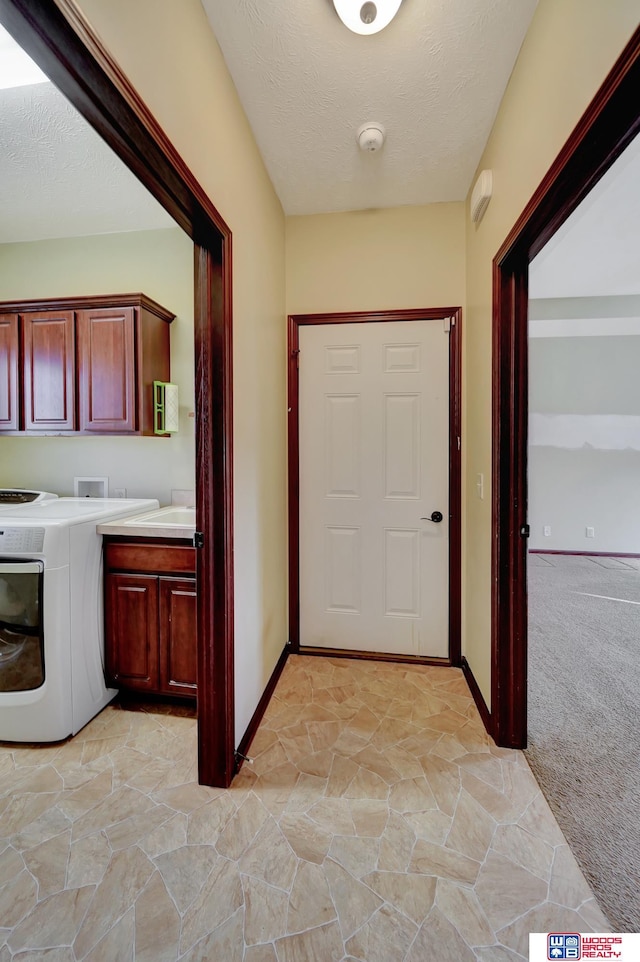 hallway with washer / dryer, a textured ceiling, light colored carpet, and baseboards