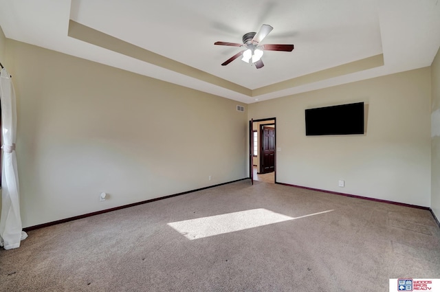 carpeted spare room with visible vents, ceiling fan, baseboards, and a tray ceiling