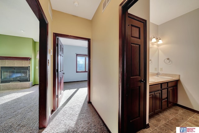 hall featuring a sink, visible vents, baseboards, and carpet