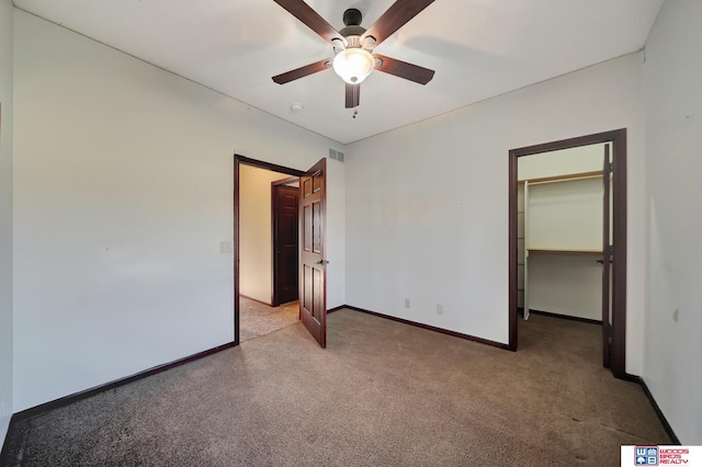 unfurnished bedroom featuring visible vents, a walk in closet, baseboards, light colored carpet, and ceiling fan