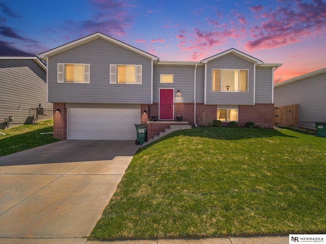 bi-level home with a lawn, brick siding, an attached garage, and driveway