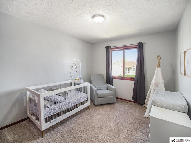 bedroom featuring a crib, baseboards, carpet, and a textured ceiling