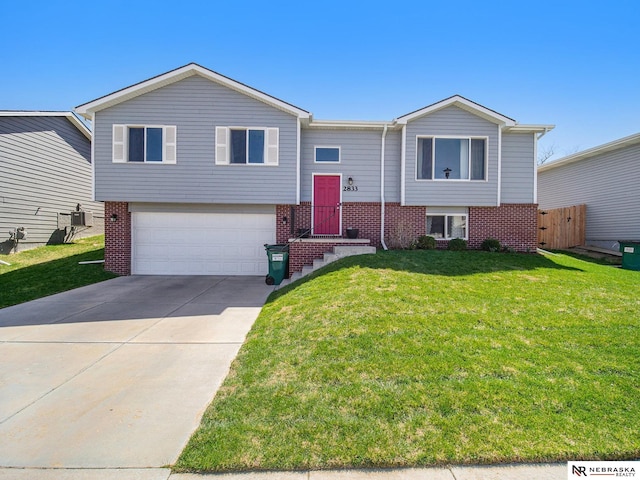 split foyer home with an attached garage, driveway, a front lawn, and brick siding