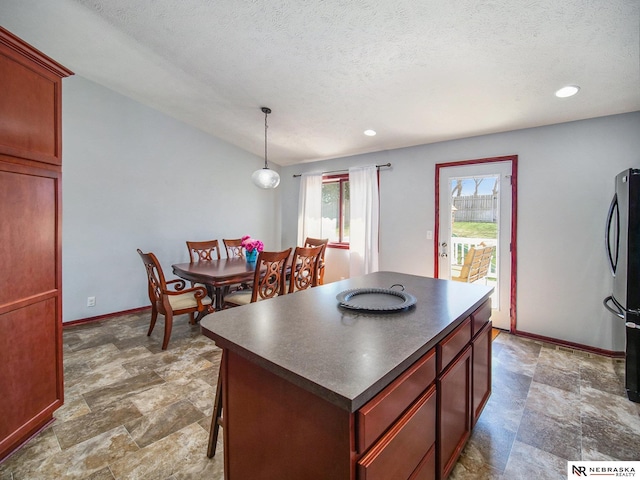 kitchen featuring freestanding refrigerator, dark countertops, stone finish flooring, and baseboards