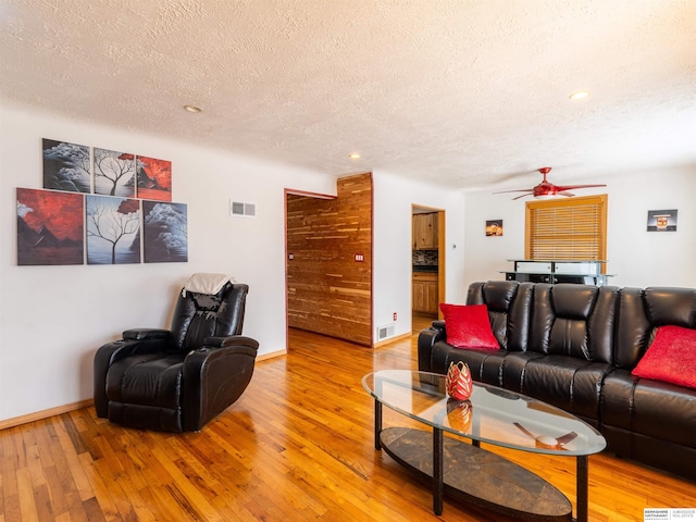 living area featuring baseboards, visible vents, a ceiling fan, wood finished floors, and a textured ceiling