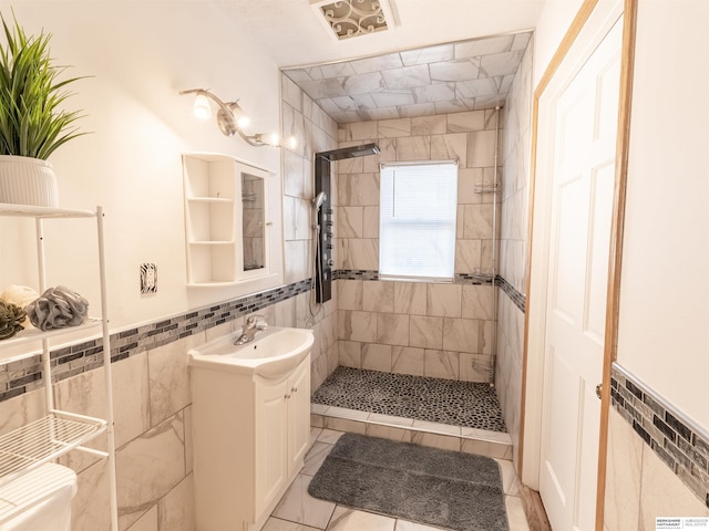 full bath with a tile shower, tile walls, and vanity