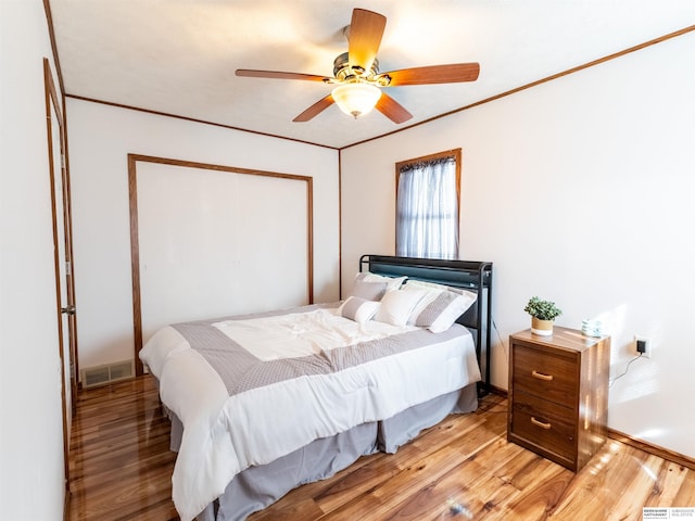 bedroom featuring ceiling fan, visible vents, baseboards, light wood-style floors, and crown molding