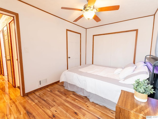 bedroom with light wood finished floors, visible vents, baseboards, ceiling fan, and ornamental molding