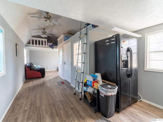 kitchen featuring baseboards, lofted ceiling, wood finished floors, black refrigerator with ice dispenser, and a textured ceiling